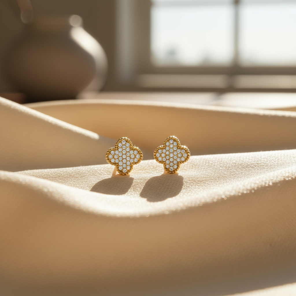 Delicate 14K gold diamond four-leaf clover earrings resting on soft silk fabric, highlighting intricate craftsmanship and sparkling pavé diamonds in natural light.