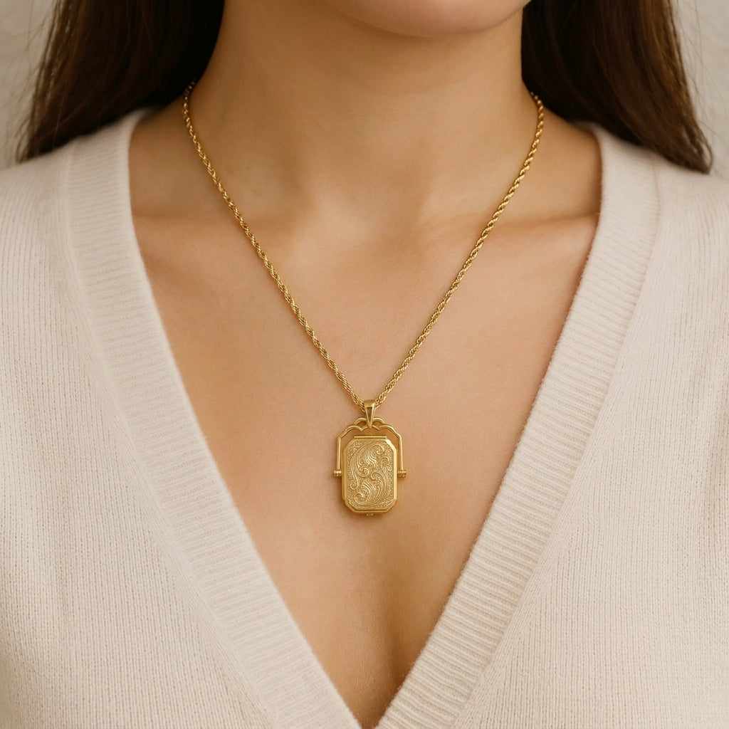 Close-up of an ornate 14K gold swivel locket on a textured surface, showing intricate filigree details against a refined jewelry studio background.