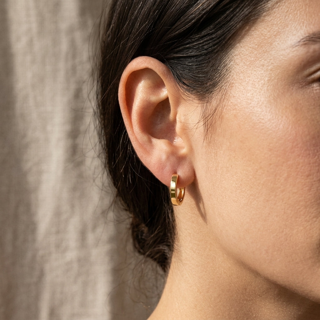 High-resolution image of 14k gold huggie hoop earring on textured linen, featuring warm lighting that emphasizes the gold tone and surface details.