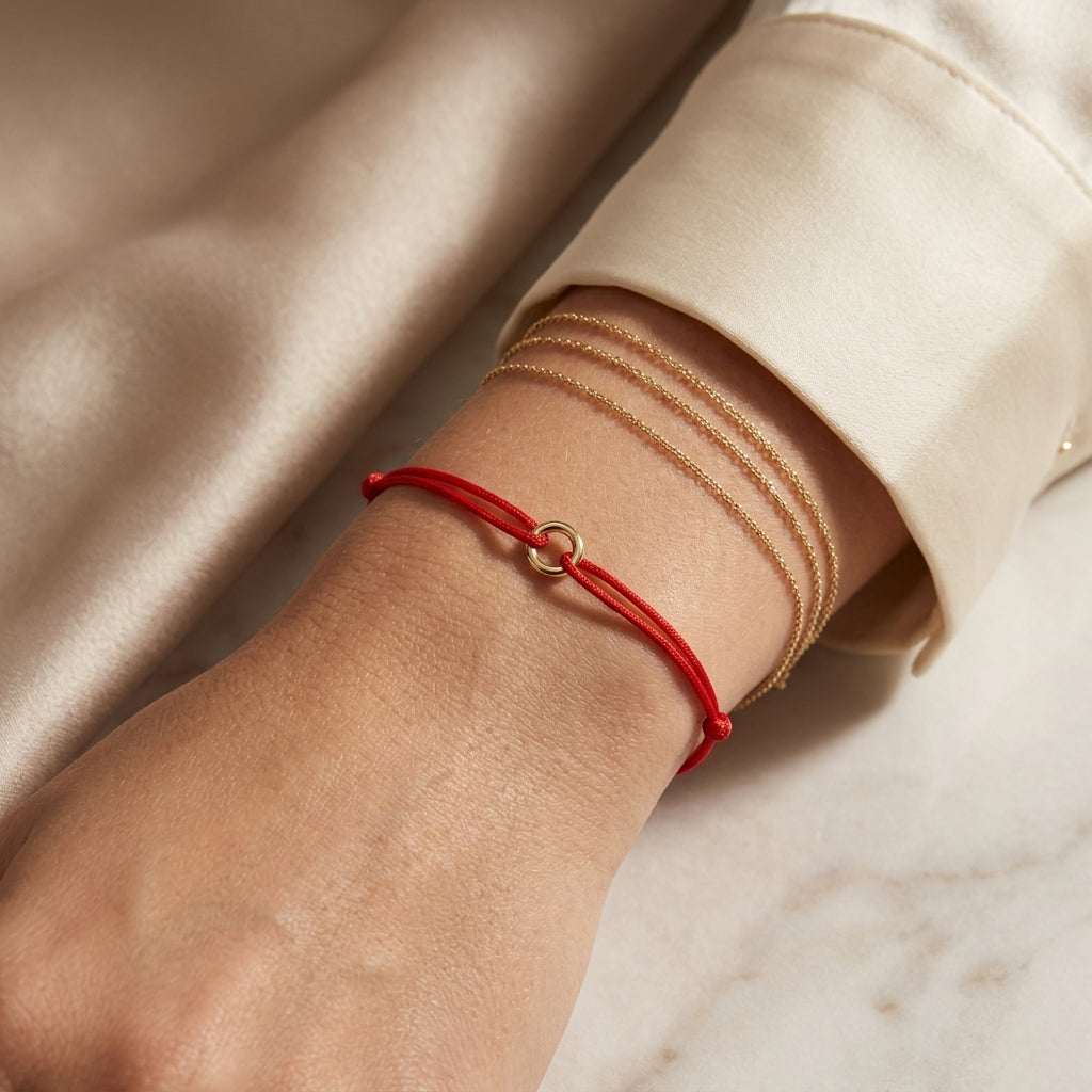 Close-up of a small 7mm gold circle charm on a red cord bracelet, highlighting the micro-texture and luxury of 14K solid gold.